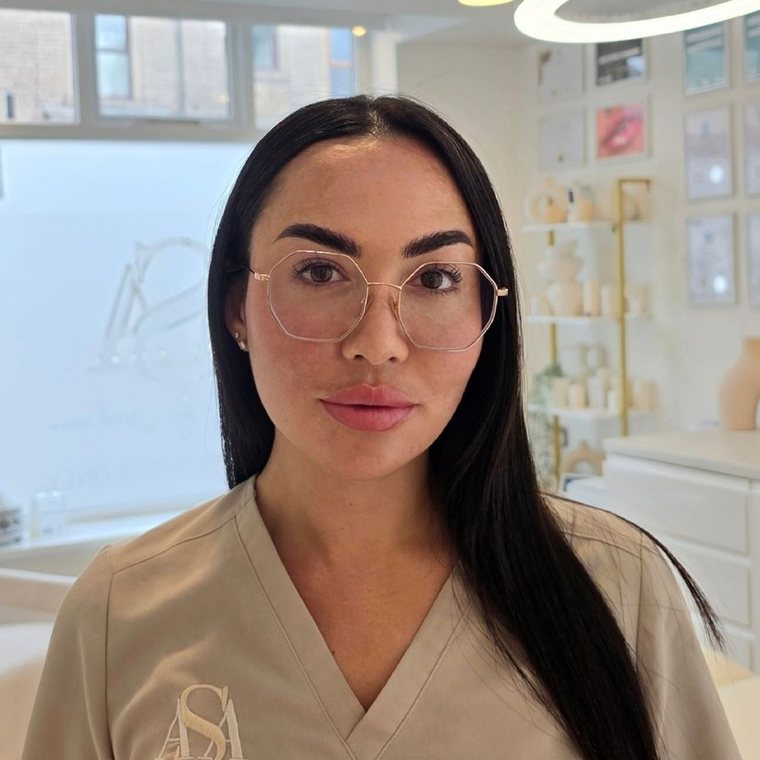 Sarah Ann Roberts in her Oldham clinic, wearing ASA branded scrubs, with her framed certificates on the wall behind her.